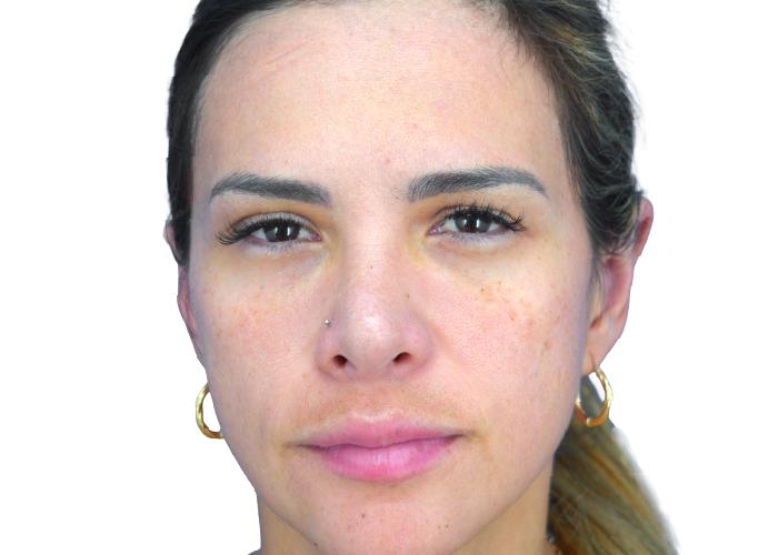 Close-up of a light-skinned woman with freckles, a nose stud, gold hoop earrings, and a neutral expression against a white background.