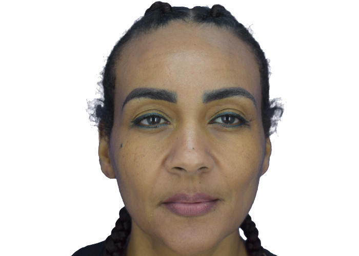 Close-up portrait of a woman with braided hair, bold eyebrows, yellow eye makeup, and neutral lips, looking at the camera.