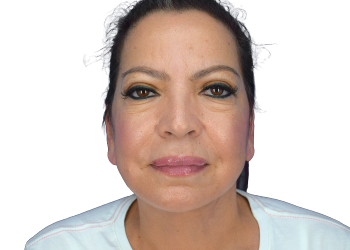 Close-up of a middle-aged woman facing the camera with dark hair, makeup (smoky eyes, pink lips), wearing a light blue top, neutral expression.